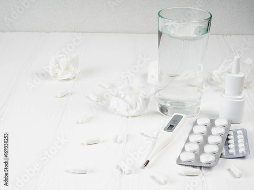 a lot of pills on white wooden background, glass of water, pills in blister packs, electronic thermometer , copy space for text, concept of medicine and health