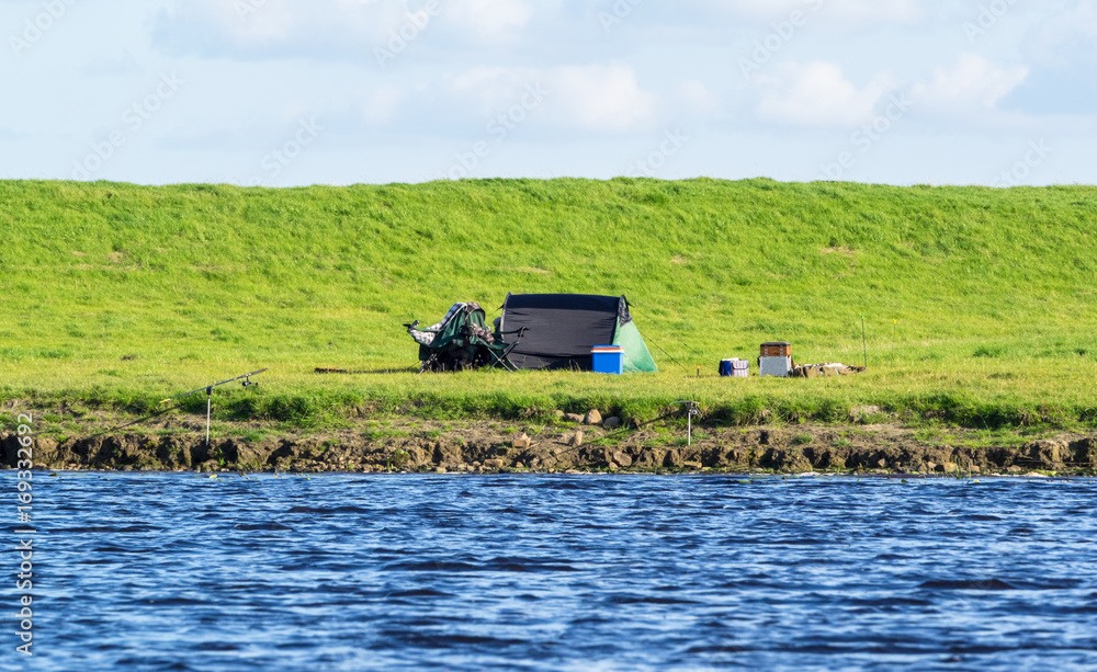 Fototapeta premium Angelstelle mit Angel und Zelt am Ufer von einem Fluss