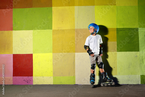 Cute little athletic boy on roller standing against the green yellow graffiti wall