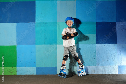 Cute little athletic boy on roller standing against the blue graffiti wall