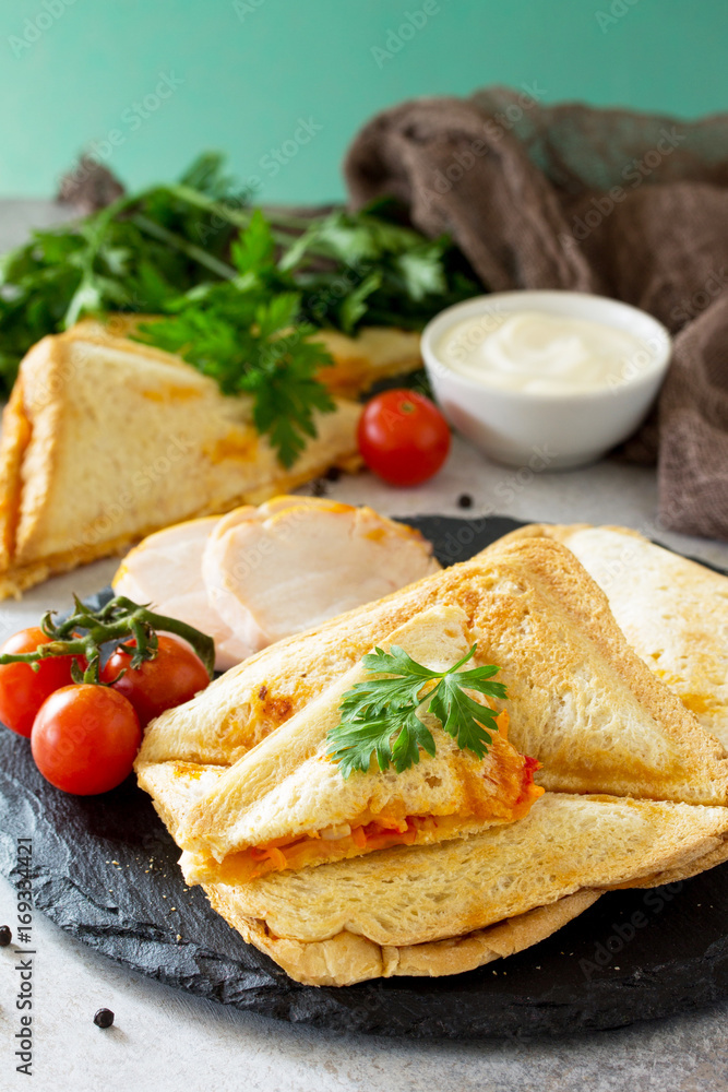 Pressed and toasted double sandwich with chicken, Korean carrots, cheese and tomatoes on a gray stone or slate. Pressed and toasted double sandwich with chicken, Korean carrots, cheese and tomatoes on a gray stone or slate.