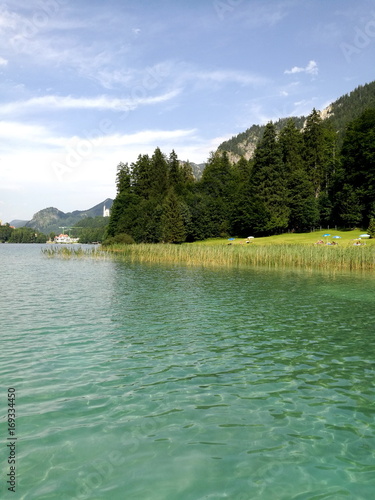 Grüne Liegewiese mit Uferschilf am idyllisch gelegenen Alpseebad am Alpsee mit Blick auf Schloß Neuschwanstein im Sommer bei Sonnenschein in Schwangau bei Füssen im Ostallgäu im Freistaat Bayern photo