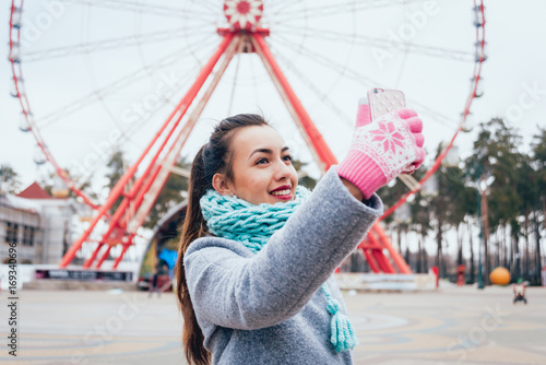 Beautiful girl taking selfie at the background of a Ferris wheel