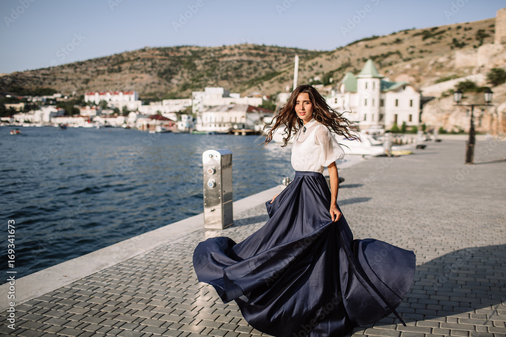 Beautiful girl walking on the pier by the sea near the yacht, boats in the blue long dress Beautiful girl walking on the pier by the sea near the yacht, boats in the blue long dress