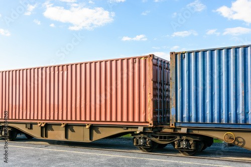 Two cargo containers on a flat car train parked in a rail terminal.