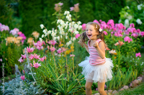 happy little girl rejoices and jumps on a lawn near flowers, it is a lot of emotions