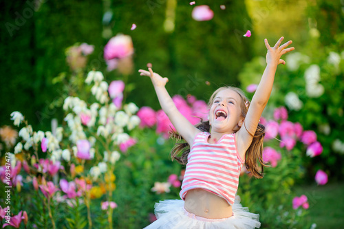 happy little girl ralutsya and jumps on a lawn near flowers  throws petals