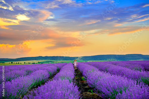 Happy girl in platitse rejoices and runs in the lavender field at sunset