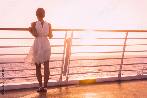 Cruise ship vacation woman luxury travel watching sunset over ocean . Elegant lady in white dress on deck enjoying view of famous holiday destination. Girl on honeymoon getaway happy relaxing.