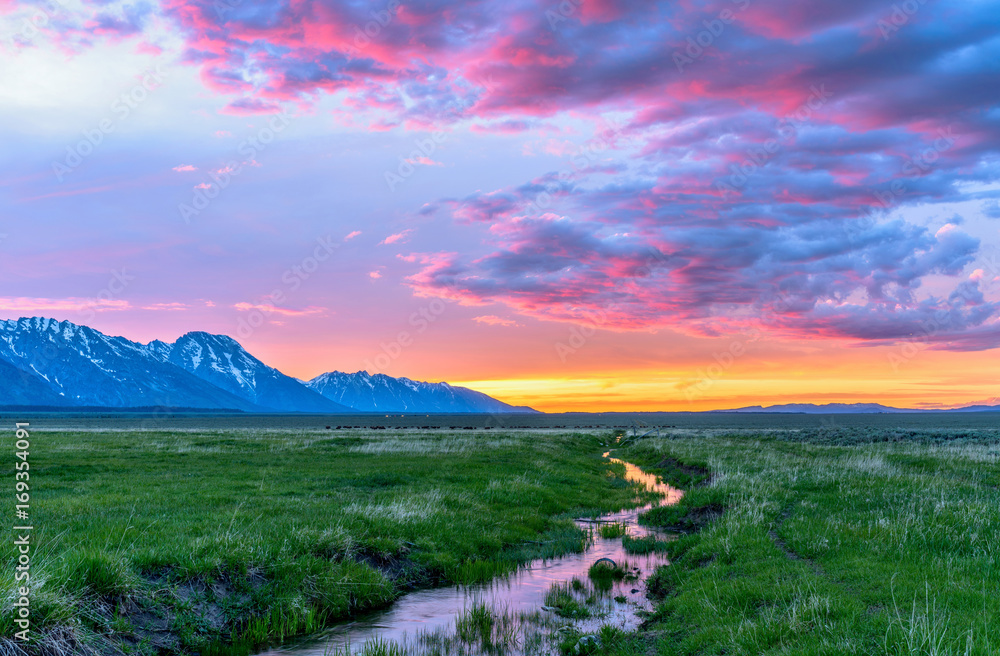 Sunset Mountain Meadow - Colorful spring sunset at a green mountain field with a winding stream near Mormon Row historic district in Grand Teton National Park, Wyoming, USA.