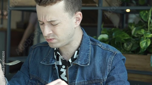 Stylish boy looks unhappy while eating unfresh salad in the cafe, steadycam shot
 photo