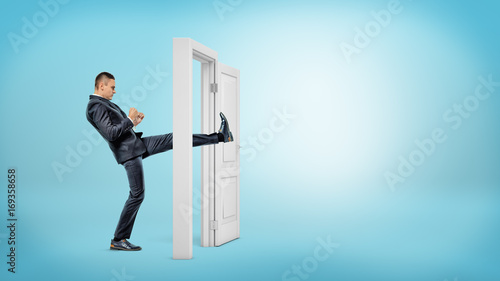 Fotografía A businessman in side view kicks a small white door open with his leg on blue backgrounds