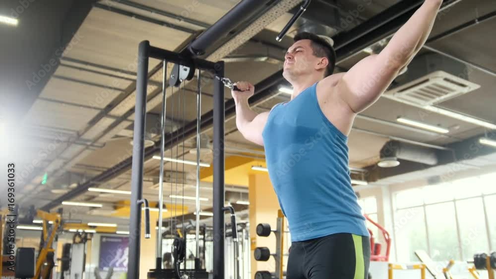 Bodybuilder training in the gym - young muscular man perform training for biceps, slider shot Bodybuilder training in the gym - young muscular man perform training for biceps, slider shot