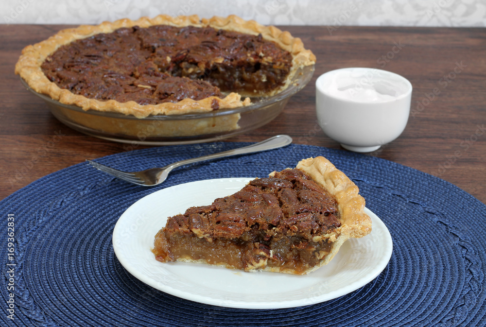 Pecan pie slice with whole pie in background.