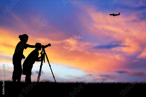 Silhouette of mother and son using camera shooting airplane during the sky sunset background