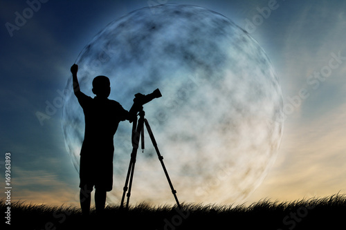 Silhouette of boy using camera shooting moon