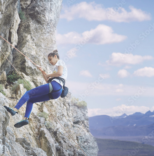 young cheerful woman climbs on the cliff. rock climber Learns to climb rocks on a rocky wall. woman makes hard move and looking up