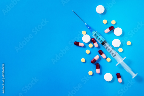 Medical preparations, pills and capsules and syringe lie on blue background. Copy space