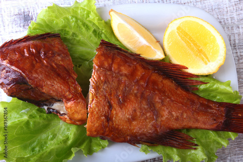 Smoked fish and lemon on green lettuce leaves on Wooden cutting board isolated on white background. photo