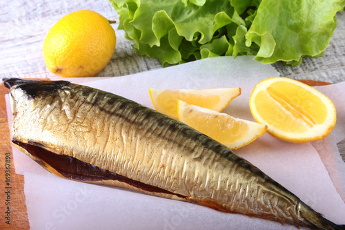 Smoked mackerele and lemon on green lettuce leaves on Wooden cutting board isolated on white background.