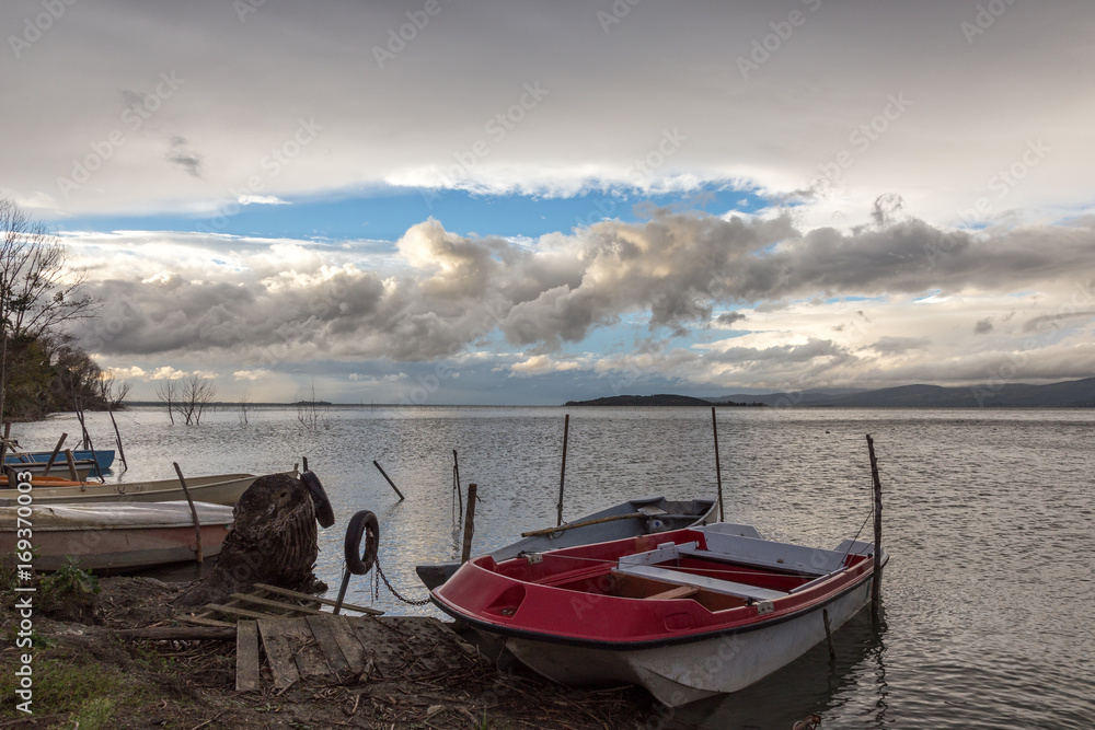 Some small fishing boat on a lake, beneath a cloudy, moody sky, with some blue openings