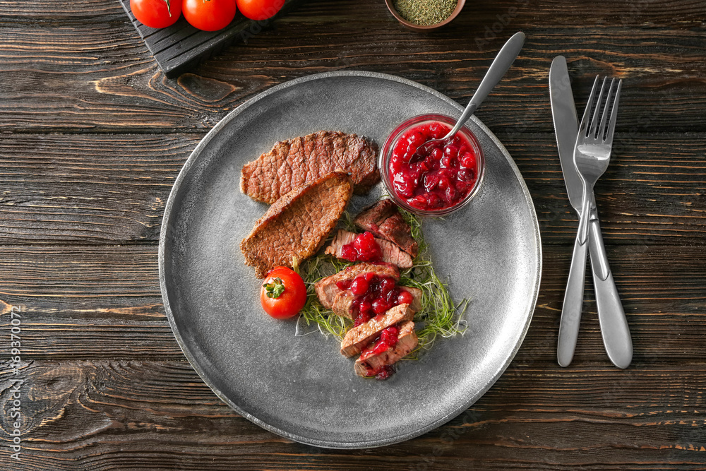Sliced steak served with cranberry sauce on metal plate
