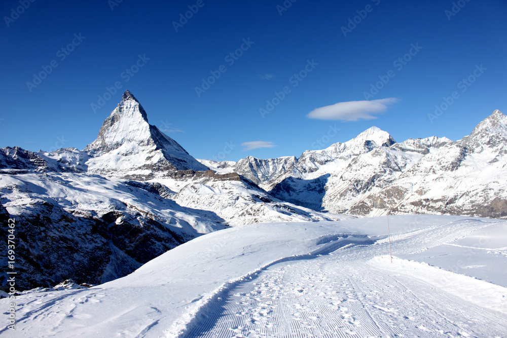 Scenic view on snowy Matterhorn peak in sunny day with blue sky and some clouds in background