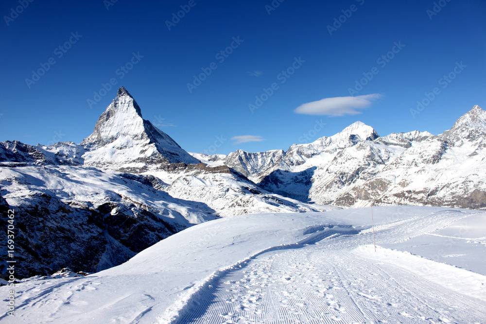 Scenic view on snowy Matterhorn peak in sunny day with blue sky and some clouds in background Scenic view on snowy Matterhorn peak in sunny day with blue sky and some clouds in background
