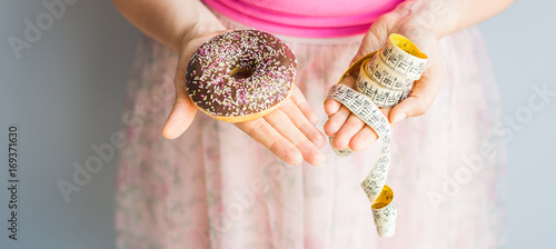 Close-up of woman's hands holding a donut and a measuring tape. The concept of healthy eating. Diet.