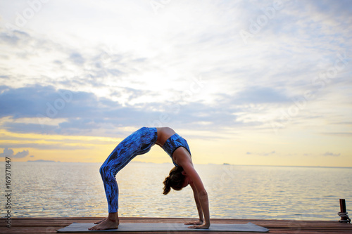 Young woman practicing yoga on the sunset beach