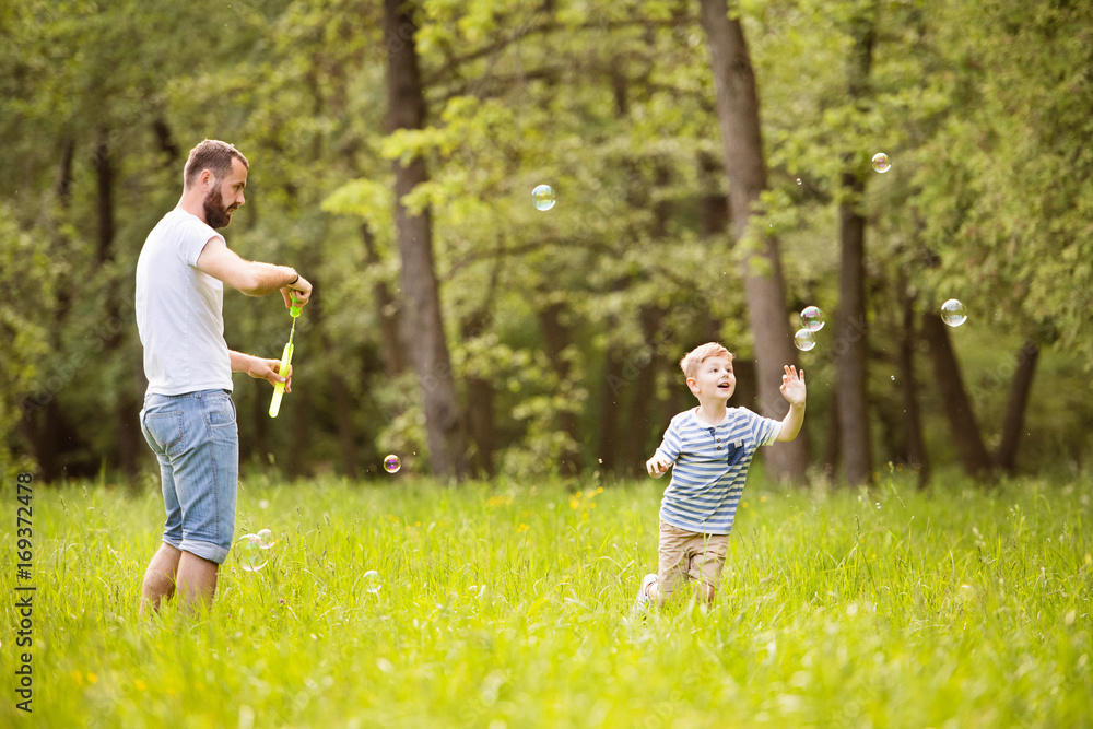 Hipster father and son blowing bubbles outdoors in park. Hipster father and son blowing bubbles outdoors in park.
