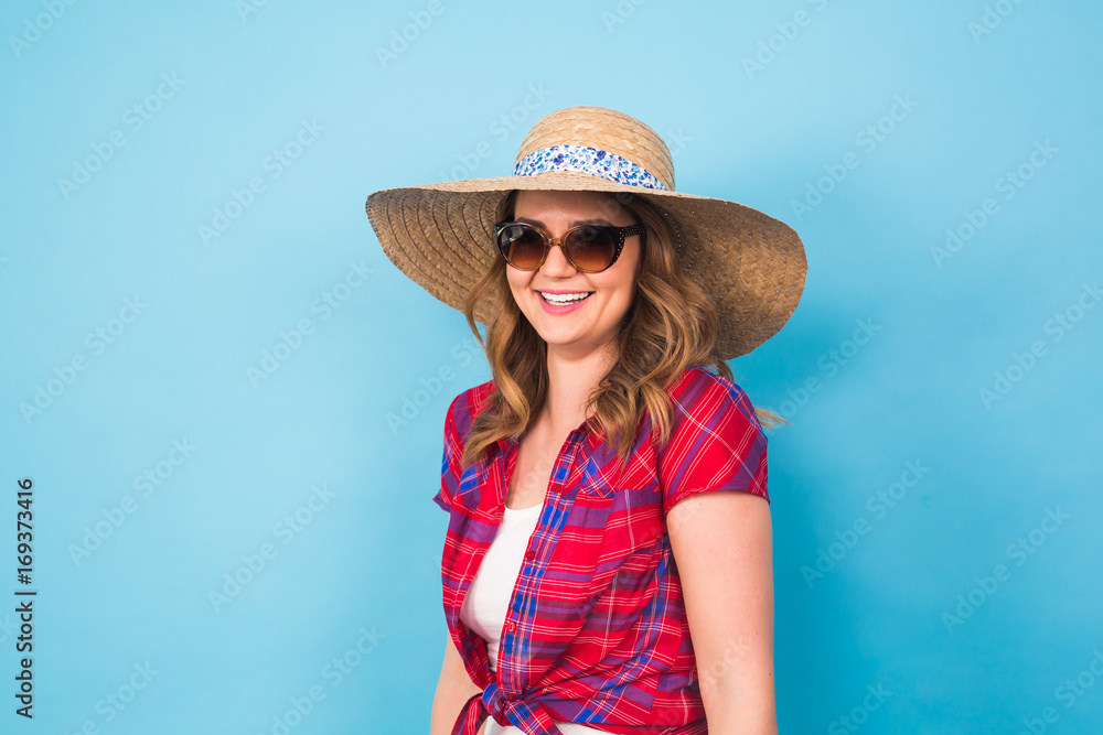 Beautiful young woman wears in summer dress and straw hat is laughing on blue background with copy space