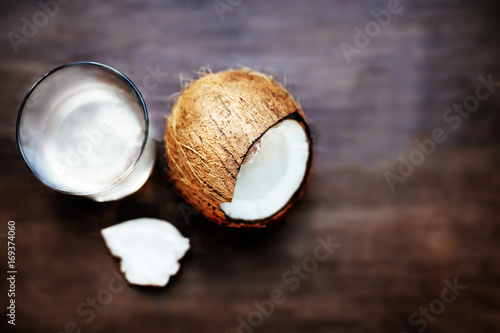 Coconut Water in a glass and cracked coco nut on dark wooden background with copyspace