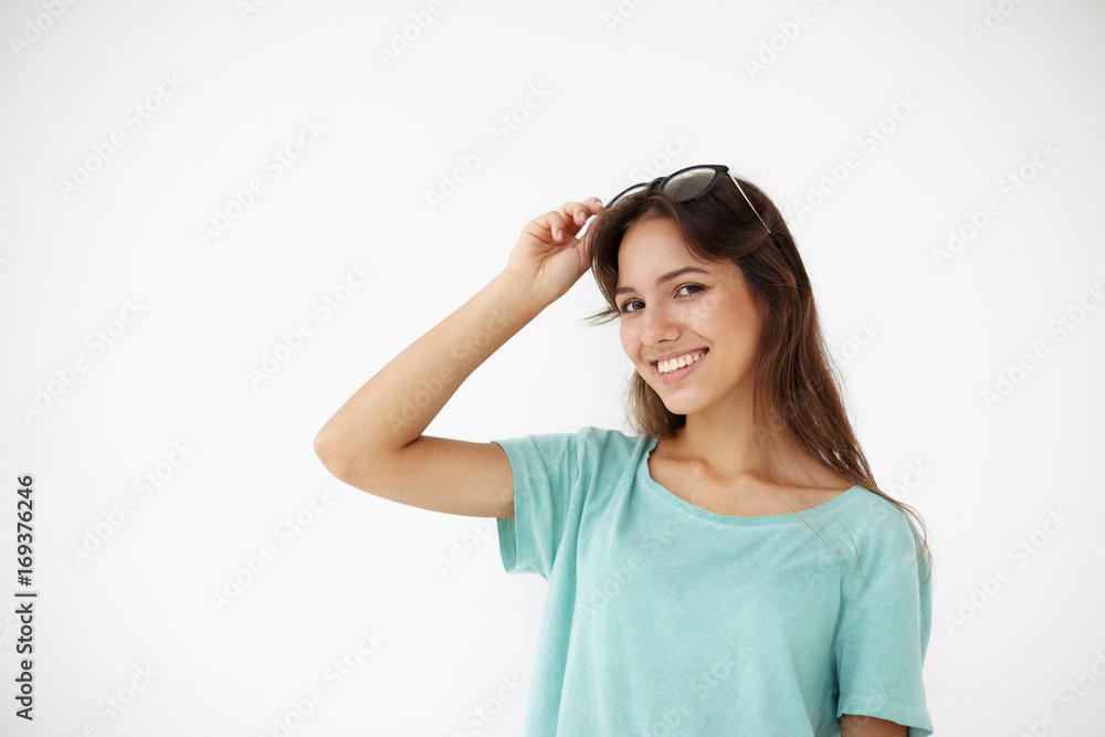 Positive human facial expressions, emotions, feelings, attitude and reaction. Gorgeous smiling young female with long brown hair wearing casual t-shirt looking at camera, adjusting shades on her head Positive human facial expressions, emotions, feelings, attitude and reaction. Gorgeous smiling young female with long brown hair wearing casual t-shirt looking at camera, adjusting shades on her head