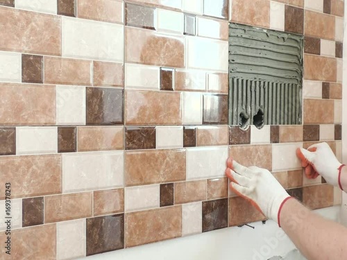 The tiler's hands are installing a tile with holes for electric boxes.
