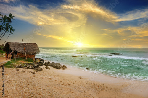old fisherman's hut on shore of picturesque ocean and beautiful sunset