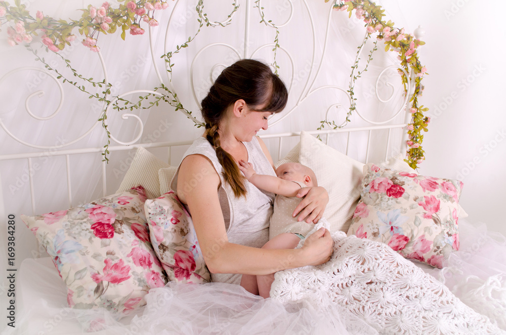Breastfeeding baby. Young mother holding her newborn child. Mom nursing baby. Woman and new born boy in white bedroom.