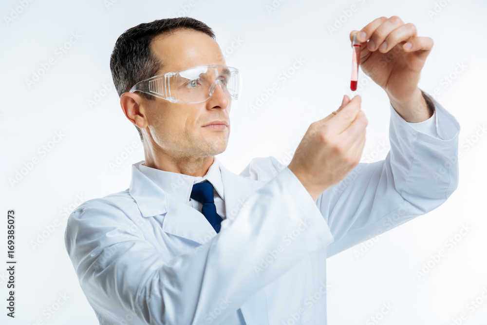 Intellectual doctor looking at test tube with blood sample Intellectual doctor looking at test tube with blood sample