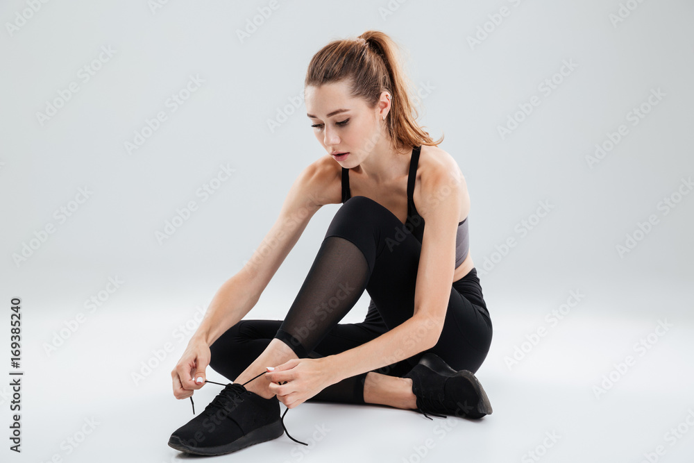 Young sportswoman sitting and tying her shoelaces Young sportswoman sitting and tying her shoelaces