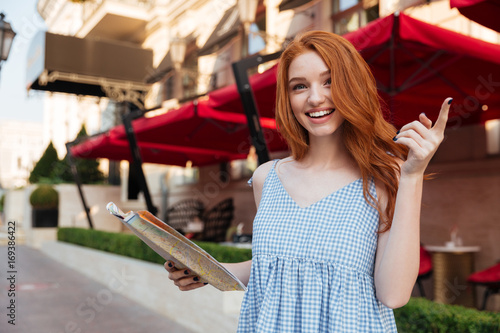 Cheerful pretty girl with long red hair holding map