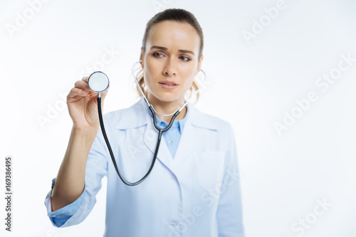 Focused female looking doctor listening to heart with stethoscope