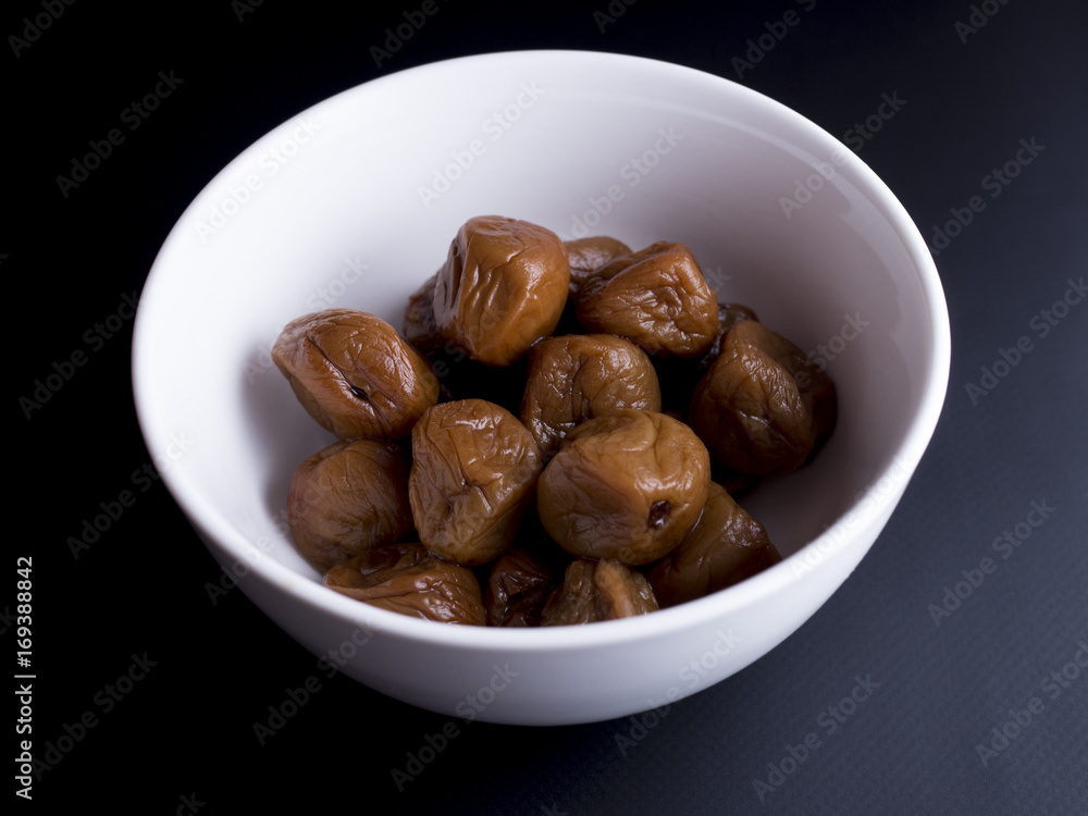 Umeboshi plums from Japan in white bowl, fermented and salted and placed in a honey syrup. Isolated on black background Umeboshi plums from Japan in white bowl, fermented and salted and placed in a honey syrup. Isolated on black background