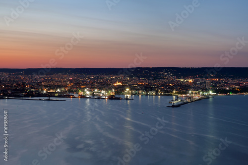 Night lights from the city and the sea port in Varna, Bulgaria at twilight with beautiful striped sky and water