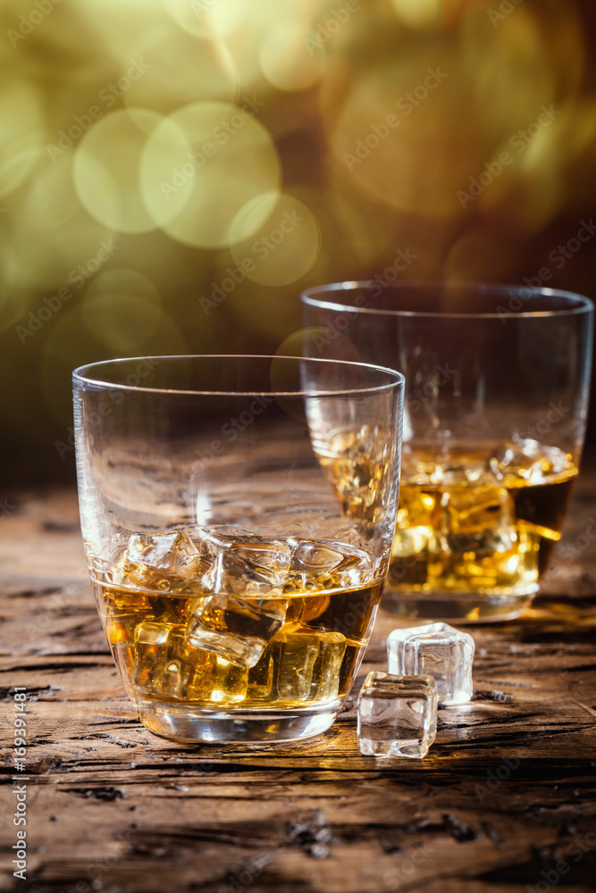 Whiskey with ice in glasses on rustic wood background Whiskey with ice in glasses on rustic wood background