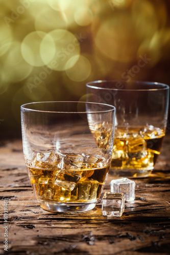 Whiskey with ice in glasses on rustic wood background