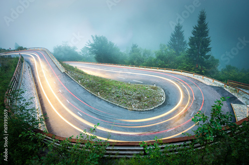 Winding mountain road with car lights. Foggy wet weather and low visibility. Alps, Slovenia.