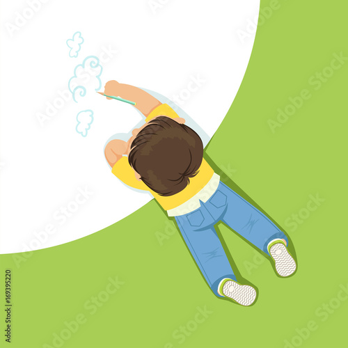 Little boy lying on his stomach and drawing clouds using pencil, top view of child on the floor