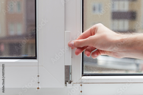 Handyman repairs plastic window with a hexagon. Workman adjusts the operation of the plastic window.