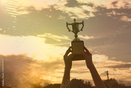 silhouette hand holding winner trophy cup in a championship with sky sunset.