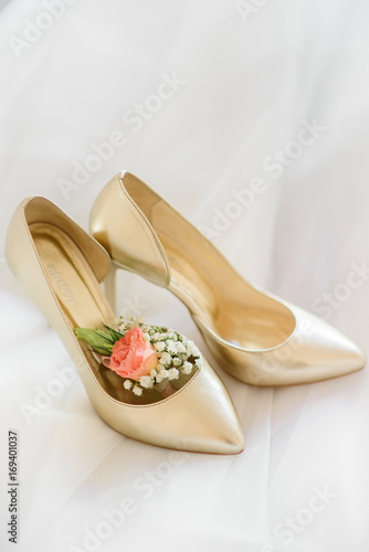 Little boutonniere made of rose lies in golden wedding shoes